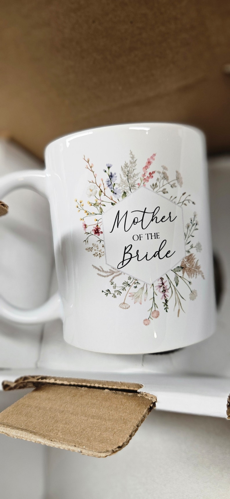 May include: White ceramic mug with a floral design and the text "Mother of the Bride" in black lettering.