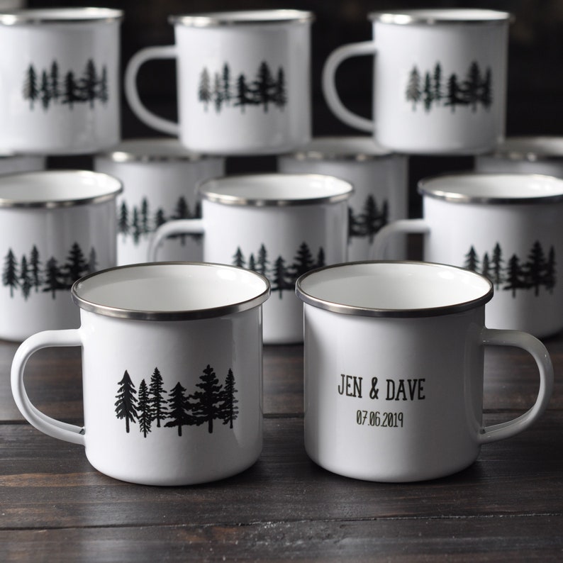 K&ouml;nnte beinhalten: Set aus wei&szlig;en Emailletassen mit schwarzen Wald-Silhouetten-Designs. Einige Tassen haben den Text "Jen & Dave 07.06.2019" aufgedruckt.