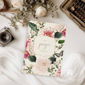May include: A floral-patterned journal with the text "My Prayer Journal" in a decorative frame. The cover features pink, white, and red flowers with green leaves on a cream background. A black and white butterfly is also visible.