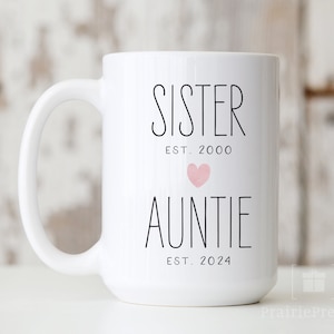 May include: White ceramic mug with black text that reads "Sister Est. 2000" with a pink heart and "Auntie Est. 2024".