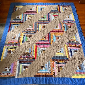May include: A brown and beige quilt with a blue border. The quilt is made of many different fabrics and has a log cabin pattern.