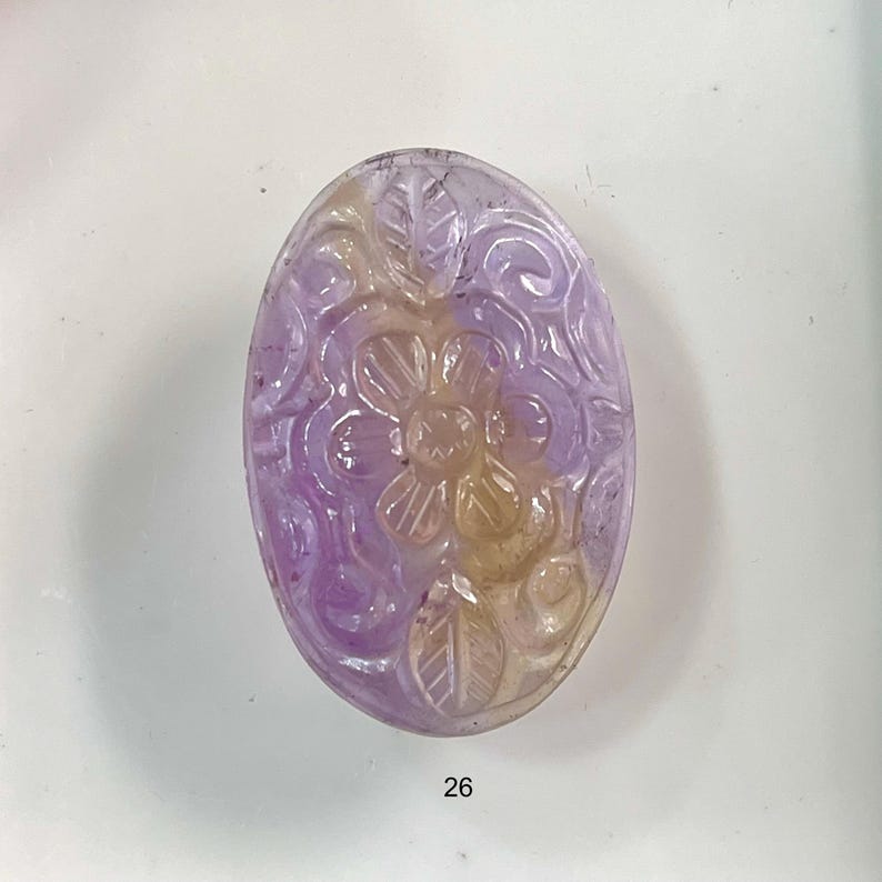 Puede incluir: Un colgante de piedra ovalada tallada con un dise&ntilde;o floral. La piedra es una mezcla de morado y amarillo.