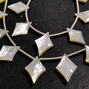 May include: Strands of iridescent, diamond-shaped beads. The beads are strung on thin, silver-colored wire. The beads have a pearlescent sheen, reflecting light with hints of yellow and blue. Ideal for jewelry making.