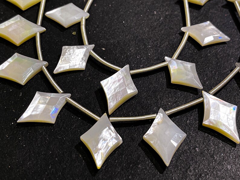 May include: Strands of iridescent, diamond-shaped beads. The beads are strung on thin, silver-colored wire. The beads have a pearlescent sheen, reflecting light with hints of yellow and blue. Ideal for jewelry making.