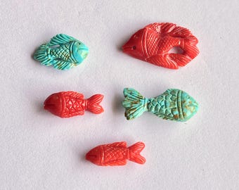May include: Five carved fish figurines in shades of red and turquoise. The fish have detailed scales and fins. The turquoise fish have a mottled appearance. The red fish are a solid color. The figurines are arranged on a white surface.