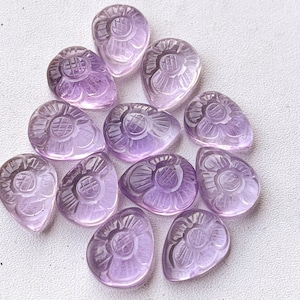 Könnte beinhalten: Eine Sammlung von 12 Amethyst-Blumenschnitzereien in Tropfenform. Die Schnitzereien sind helllila und haben komplizierte Details.