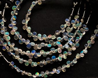 May include: A strand of iridescent opal beads in a teardrop shape. The beads are strung on a silver wire and are arranged in a circular pattern.