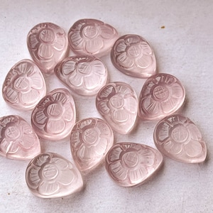 Könnte beinhalten: Eine Sammlung von 14 tropfenförmigen Anhängern aus rosa Rosenquarz mit geschnitzten Blumendesigns.
