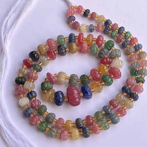 May include: A multi-colored gemstone necklace with faceted beads in shades of pink, blue, green, and yellow. The beads are strung on a gold-colored thread.