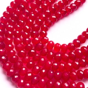 Könnte beinhalten: Eine Strähne aus leuchtend roten facettierten Edelsteinperlen. Die Perlen sind rund und haben eine glatte, polierte Oberfläche.