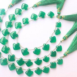 May include: A strand of green gemstone beads with a heart shape. The beads are strung on a gold wire and have a tassel at each end.