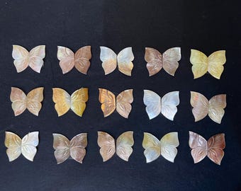 May include: A collection of 15 mother of pearl butterfly shapes in various shades of brown, white, and beige. The butterflies are arranged in three rows of five.