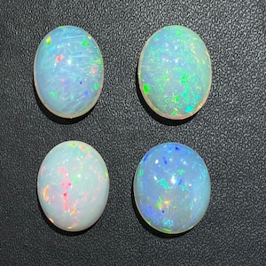 Può includere: Quattro opali bianche di forma ovale con colori arcobaleno iridescenti. Le opali sono posizionate su uno sfondo grigio scuro.