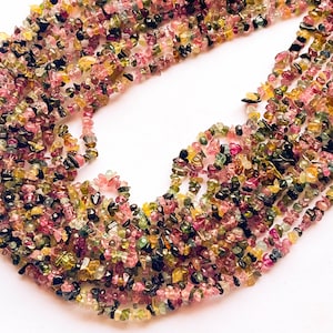 Puede incluir: Primer plano de hebras de chips de piedras preciosas de turmalina de colores. Los chips son una mezcla de rosa, verde, amarillo y negro, creando un aspecto vibrante y natural. Ideal para la fabricación de joyas.