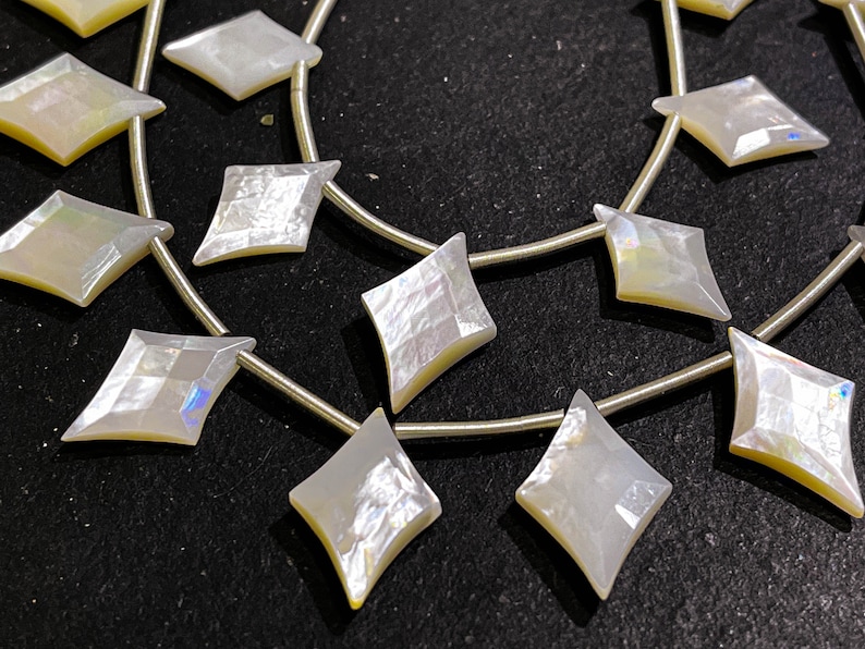 May include: Strands of iridescent, diamond-shaped beads. The beads are a pearly white with subtle yellow and blue hues, strung on thin, silver-colored wire. The beads are arranged in a repeating pattern.