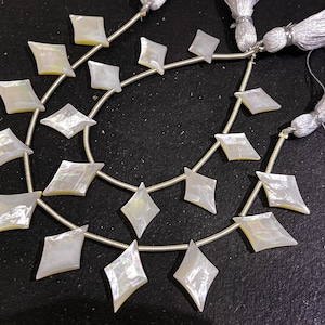 May include: Strands of iridescent, diamond-shaped mother-of-pearl beads. Each bead is strung on a silver-colored wire, with a tassel at the end. The beads have a pearlescent sheen, reflecting light with a subtle rainbow effect. Ideal for jewelry making.