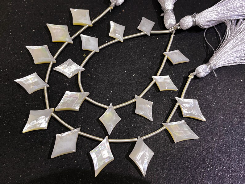 May include: Strands of iridescent, diamond-shaped mother-of-pearl beads. Each bead is strung on a silver-colored wire, with a tassel at the end. The beads have a pearlescent sheen, reflecting light with a subtle rainbow effect. Ideal for jewelry making.