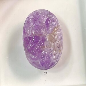 Puede incluir: Una piedra preciosa de amatista tallada con un dise&ntilde;o floral. La piedra preciosa es de color p&uacute;rpura claro y tiene un acabado liso y pulido.