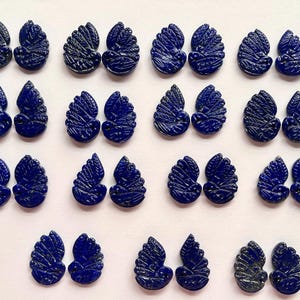 Könnte beinhalten: Vierundzwanzig dunkelblaue Edelstein-Cabochons in Form eines stilisierten Blattes. Jeder Cabochon hat ein detailliertes, geschnitztes Design.