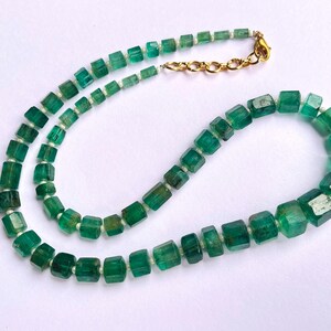 May include: A necklace made of green emerald beads, each bead is a square shape. The necklace has a gold clasp.