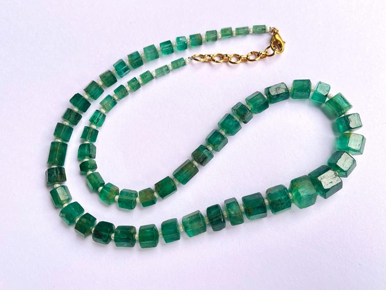 May include: A necklace made of green emerald beads, each bead is a square shape. The necklace has a gold clasp.