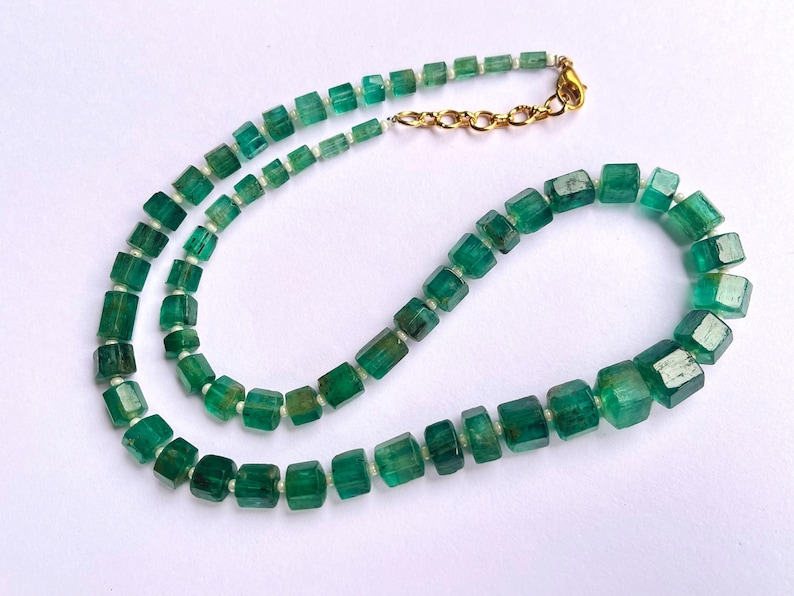 May include: A necklace made of green emerald beads, each bead is a square shape. The necklace has a gold clasp.