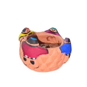 Puede incluir: Una pequeña maceta de terracota con una superficie texturizada y pintada con figuras coloridas. Las figuras llevan sombreros y ropa de diferentes colores.