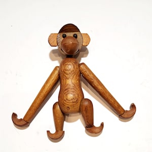 May include: A wooden monkey toy with articulated limbs and a brown and natural wood finish. The monkey has black eyes and a simple, stylized design.