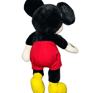 K&ouml;nnte beinhalten: Ein schwarzes und rotes Pl&uuml;sch-Mickey-Mouse-Spielzeug mit gelben Schuhen. Das Spielzeug steht auf einem wei&szlig;en Hintergrund.