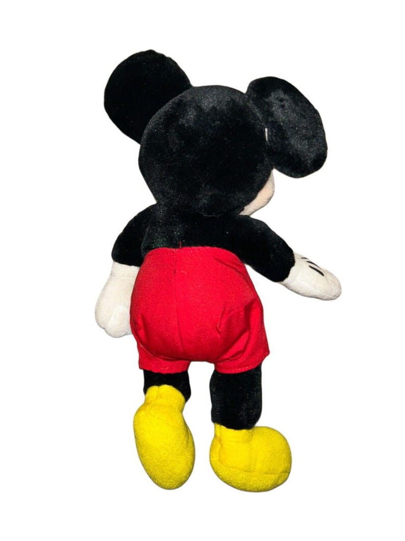 K&ouml;nnte beinhalten: Ein schwarzes und rotes Pl&uuml;sch-Mickey-Mouse-Spielzeug mit gelben Schuhen. Das Spielzeug steht auf einem wei&szlig;en Hintergrund.
