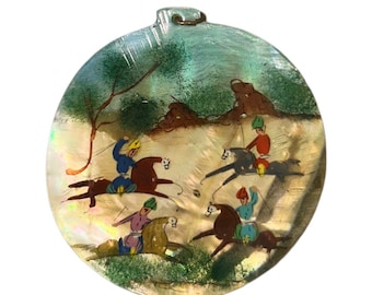May include: A round, iridescent, mother-of-pearl pendant with a painted scene of people riding horses. The pendant has a loop at the top for hanging.