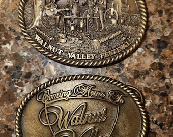 May include: Two vintage brass belt buckles featuring the text "Coming Home to Walnut Valley" and "Walnut Valley Festival 1994" with a scene of people playing music and a wagon.