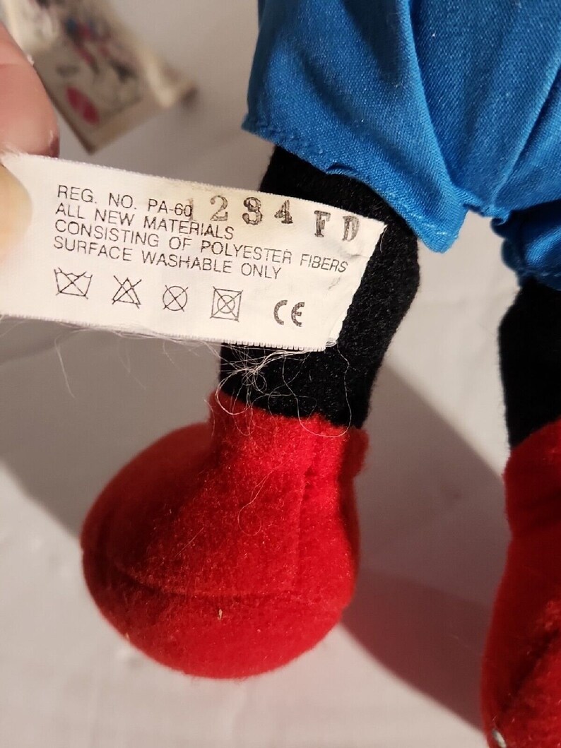 K&ouml;nnte beinhalten: Ein schwarzes und rotes Pl&uuml;schtier mit einem blauen Hemd. Das Spielzeug hat ein Etikett mit der Aufschrift "REG. NO. PA-60 284 FD ALL NEW MATERIALS CONSISTING OF POLYESTER FIBERS SURFACE WASHABLE ONLY XXCE".