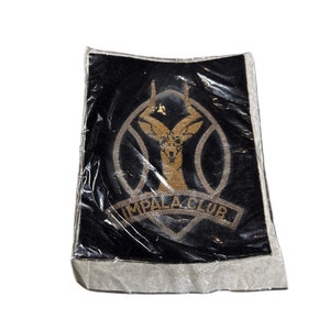 Puede incluir: Un parche de tela negro con bordado dorado de una cabeza de impala y las palabras "Impala Club".