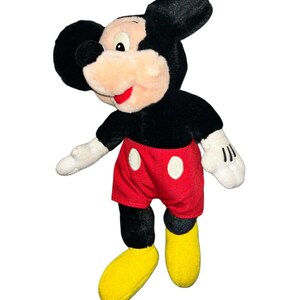 K&ouml;nnte beinhalten: Ein Pl&uuml;sch-Mickey-Mouse-Spielzeug mit schwarzem Fell, roten Shorts mit wei&szlig;en Punkten und gelben Schuhen.