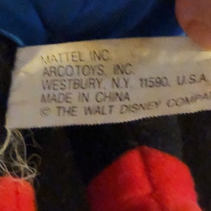 K&ouml;nnte beinhalten: Nahaufnahme eines wei&szlig;en Etiketts mit schwarzem Text, der "MATTEL INC. ARCO TOYS, INC. WESTBURY, N.Y. 11590, U.S.A MADE IN CHINA &copy; THE WALT DISNEY COMPANY" lautet.