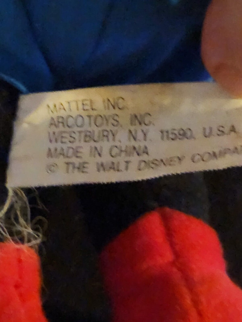 K&ouml;nnte beinhalten: Nahaufnahme eines wei&szlig;en Etiketts mit schwarzem Text, der "MATTEL INC. ARCO TOYS, INC. WESTBURY, N.Y. 11590, U.S.A MADE IN CHINA &copy; THE WALT DISNEY COMPANY" lautet.