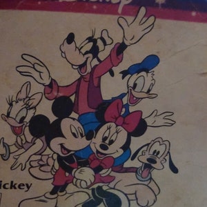 K&ouml;nnte beinhalten: Eine Vintage-Disney-Illustration mit Mickey Mouse, Minnie Mouse, Goofy, Pluto und Donald Duck. Die Figuren l&auml;cheln alle und scheinen miteinander zu interagieren. Die Illustration ist im Cartoon-Stil gehalten und auf einem hellbraunen Hintergrund gedruckt. Der Text "Disney" ist oben auf der Illustration gedruckt. Der Text "For over 18 months" ist unten auf der Illustration gedruckt. Der Text "NO. 69628" und "ASST. NO. 65383" ist unten rechts auf der Illustration gedruckt.