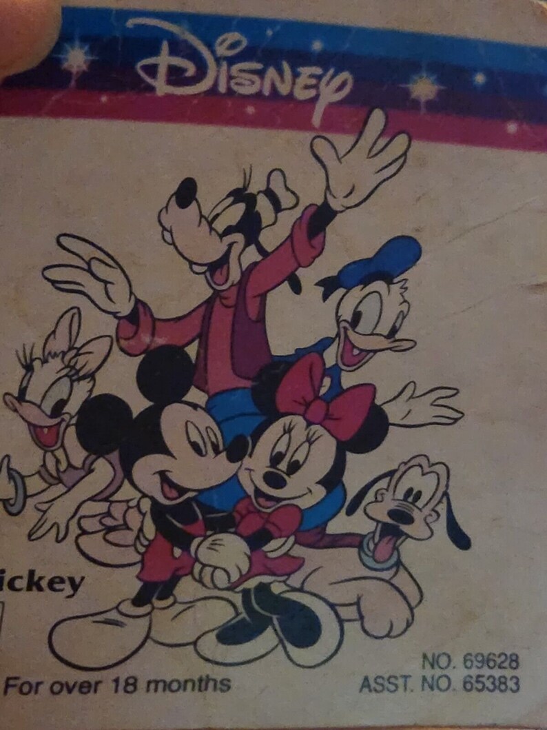 K&ouml;nnte beinhalten: Eine Vintage-Disney-Illustration mit Mickey Mouse, Minnie Mouse, Goofy, Pluto und Donald Duck. Die Figuren l&auml;cheln alle und scheinen miteinander zu interagieren. Die Illustration ist im Cartoon-Stil gehalten und auf einem hellbraunen Hintergrund gedruckt. Der Text "Disney" ist oben auf der Illustration gedruckt. Der Text "For over 18 months" ist unten auf der Illustration gedruckt. Der Text "NO. 69628" und "ASST. NO. 65383" ist unten rechts auf der Illustration gedruckt.