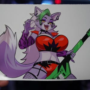 May include: A colorful sticker featuring a cartoon character with purple fur, green hair, and a red top. The character is holding a green and black guitar. The sticker has a white background and is held by a hand.