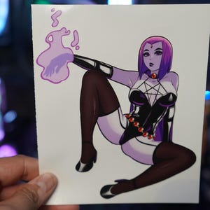 May include: A sticker featuring a stylized illustration of a character with purple skin and hair, wearing a black and white outfit with a pentagram design. The character is posed with a purple energy effect.