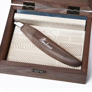 Può includere: Una scatola di legno con un interno rivestito in pelle e uno strumento di legno con una lama di metallo. La scatola contiene una varietà di motivi per esercitarsi nella scultura del legno. Lo strumento è etichettato "Ambrus".