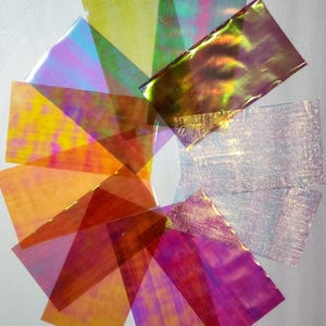 Puede incluir: Surtido de láminas de vinilo holográfico iridiscente en varios colores, incluyendo dorado, verde, azul, morado y naranja. Las láminas están dispuestas en un patrón circular.