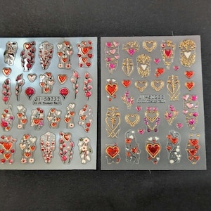 May include: Two sheets of nail art stickers with heart and floral designs. One sheet features red hearts and floral accents, while the other has gold and pink heart and floral patterns. The text "JI-5D232" is visible on one sheet.