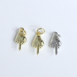 May include: Three metal hand charms, each with a finger pointing up. Two are gold-colored, and one is silver-colored. The charms are small and have a loop at the top for attaching to a necklace or bracelet. The background is white.