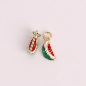 May include: Two gold-colored watermelon charms. One charm is a slice of watermelon with a green rind, white flesh, and red interior with black seeds. The other charm is a watermelon shape with red interior and black seeds.