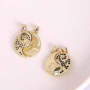 Könnte beinhalten: Zwei goldfarbene Yin-Yang-Anhänger. Ein Anhänger hat ein gepunktetes Design, der andere ein Sonnen- und Mond-Design mit schwarzen Akzenten. Beide Anhänger haben oben eine kleine Schlaufe für eine Kette.