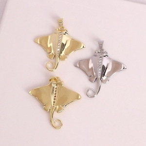 Puede incluir: Tres collares con colgantes en forma de manta raya. Dos son dorados y uno plateado. Cada colgante tiene una cola curvada y una fila de pequeñas piedras transparentes en el centro.