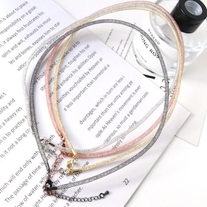 May include: A set of four tubular mesh choker necklaces in silver, rose gold, gold, and gunmetal gray tones. Each necklace features a fine metallic glitter texture, a lobster claw clasp, and an adjustable extender chain with a small round charm.