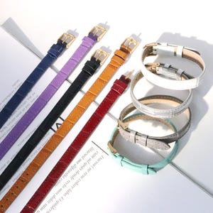 May include: An assortment of watch straps in various colors, including navy, purple, black, tan, and red. The straps have gold-colored buckles and are arranged with several watch bands in white, silver, gray, and mint green.